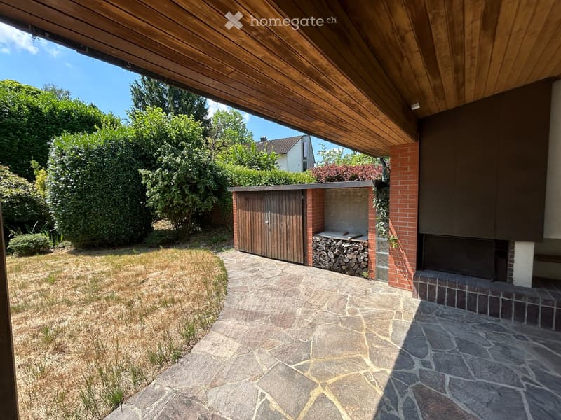 Outdoor patio area with stone paving, wooden pergola, brick barbecue, and neatly stacked firewood.
