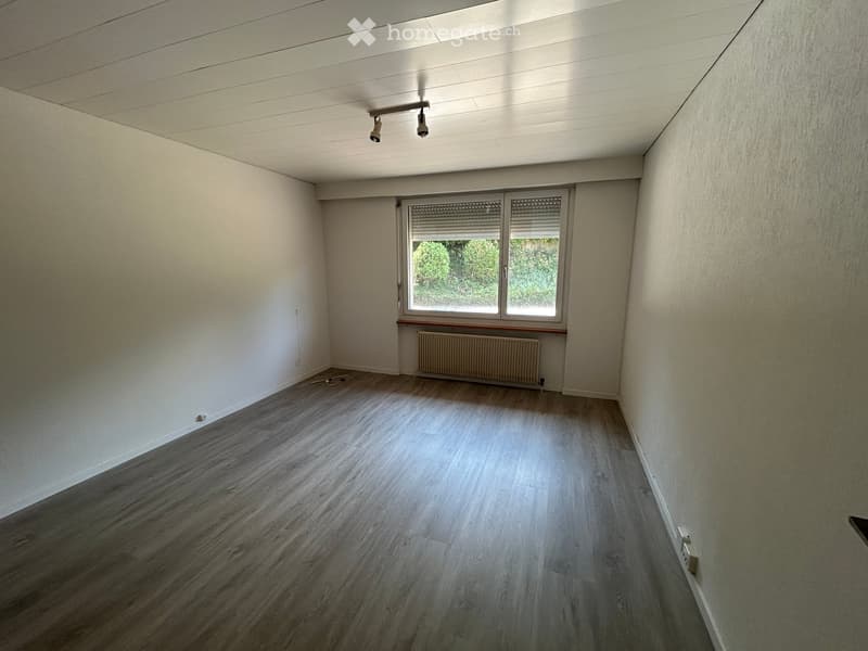 Empty room with wooden flooring, white walls, and a window with blinds. A radiator is placed under the window, and the ceiling has recessed lighting.