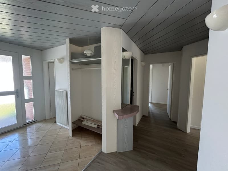 Empty hallway with wooden and tiled flooring, white walls, and several doors leading to other rooms.