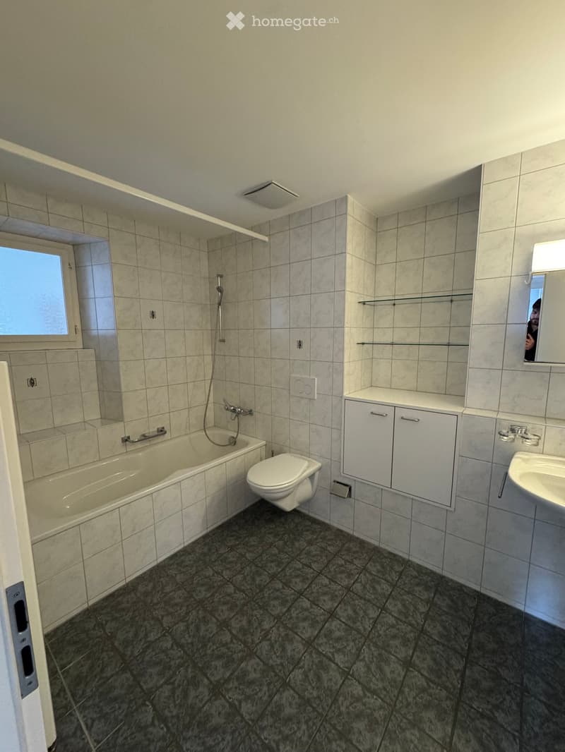Bathroom with white tiles, bathtub, toilet, sink, mirror, and shower fixtures.