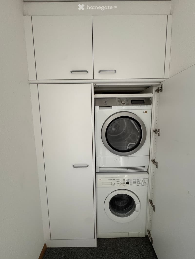 A small room with white cabinets and a built-in washing machine and dryer.