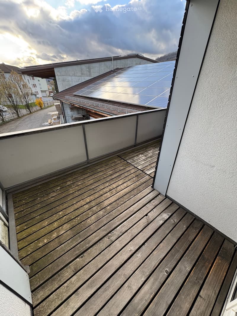 Wooden deck balcony with a view of the surrounding area, including a building with solar panels.