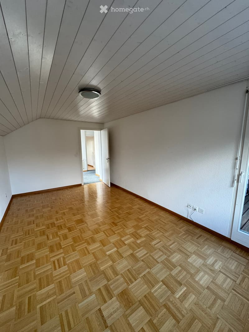 Empty room with wooden parquet flooring, white walls, and a ceiling with a ceiling light. There are two power outlets on the wall.