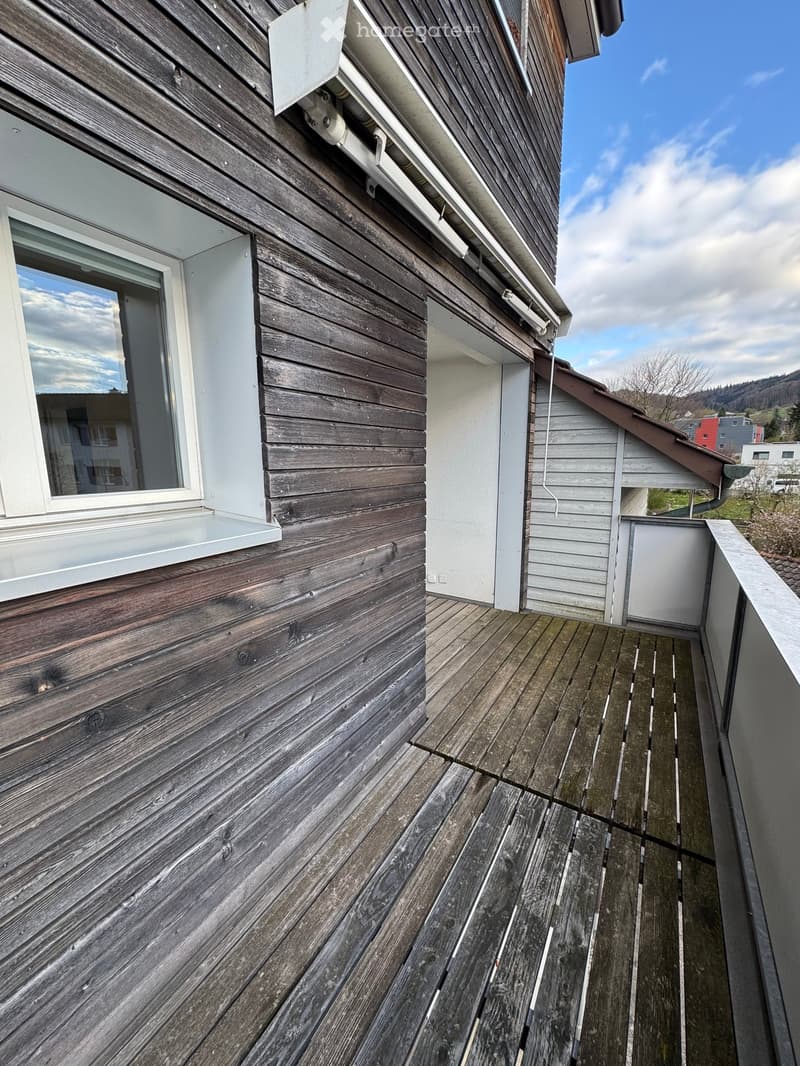 Wooden balcony with a view of the sky and distant buildings.
