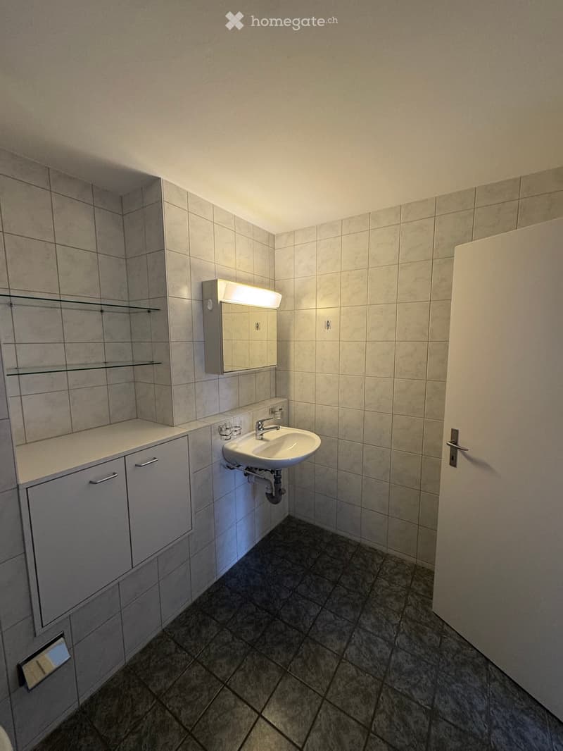 Bathroom with tiled walls and floor, a sink, mirror, and cabinets.