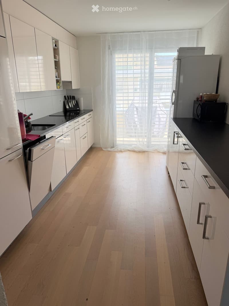 modern kitchen with white cabinets, wooden floor, black countertops, stainless steel appliances, large windows with white curtains