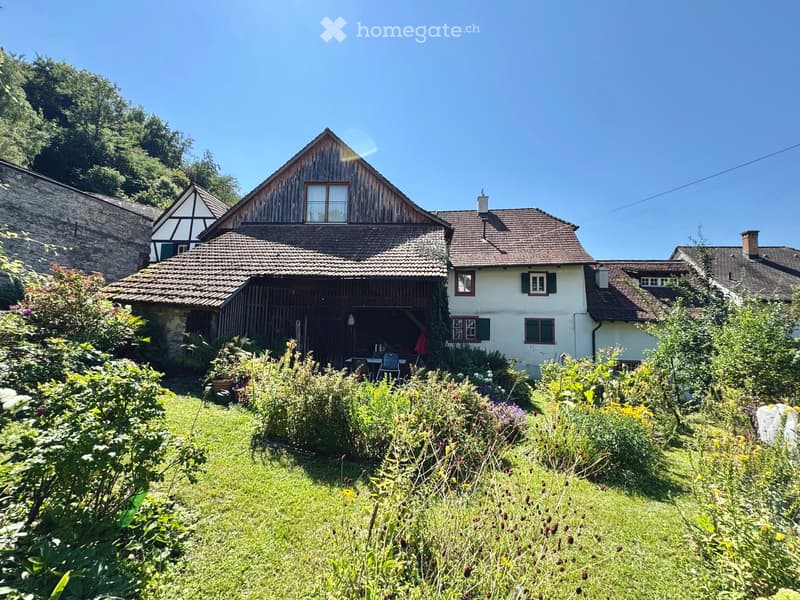 Traditional house, brown roof, white walls, surrounded by lush garden, old village background