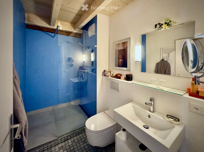 a bathroom with blue shower stall, white porcelain sink, white toilet, wooden ceiling, wall mounted power outlet, mirrors with makeup lights