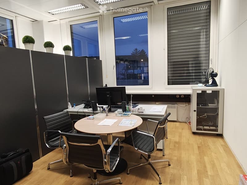 Wood floor, round table, four swivel office chairs, large windows, desktop computers, small office desk, black dividers