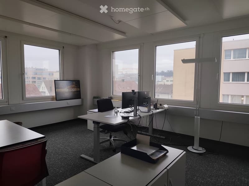 Office with desks, chairs, computer monitors, lamps, and windows providing city view