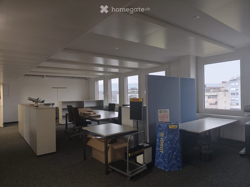 spacious office with multiple desks, blue partition screens, windows with city view, storage boxes, office equipment