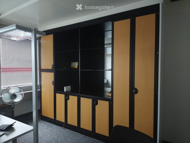 A corner with a built-in wooden and black colored unit, wooden cabinets, and a small table with a calculator