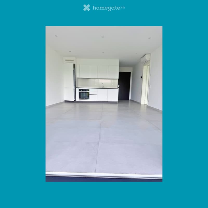 Unfurnished Room. An empty room with white walls and a gray floor. It has a modern kitchen with white cabinets, a sink, and a built-in oven. There is a black door and a white door on the right side. The room has a ceiling with recessed lighting.
