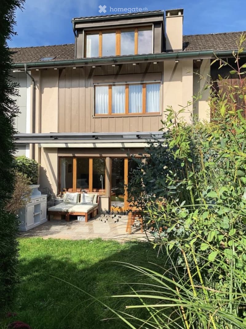 {"visible_features": ["Garden / Outdoor Area"], "type": "House", "objects": ["daybed", "cushions", "wooden table", "white cabinet", "faucet"], "description": "Two-story house with wooden exterior, large windows, and a patio with a daybed and cushions.", "