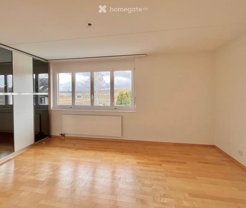 Empty room with wooden floors, white walls, large windows, and a white radiator. No furniture or equipment.