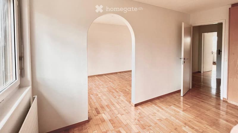 Empty room with wooden floors, white walls, arched doorway, and an open door leading to another room.