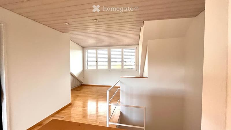 Empty room with white walls, wooden floor, and a white staircase.