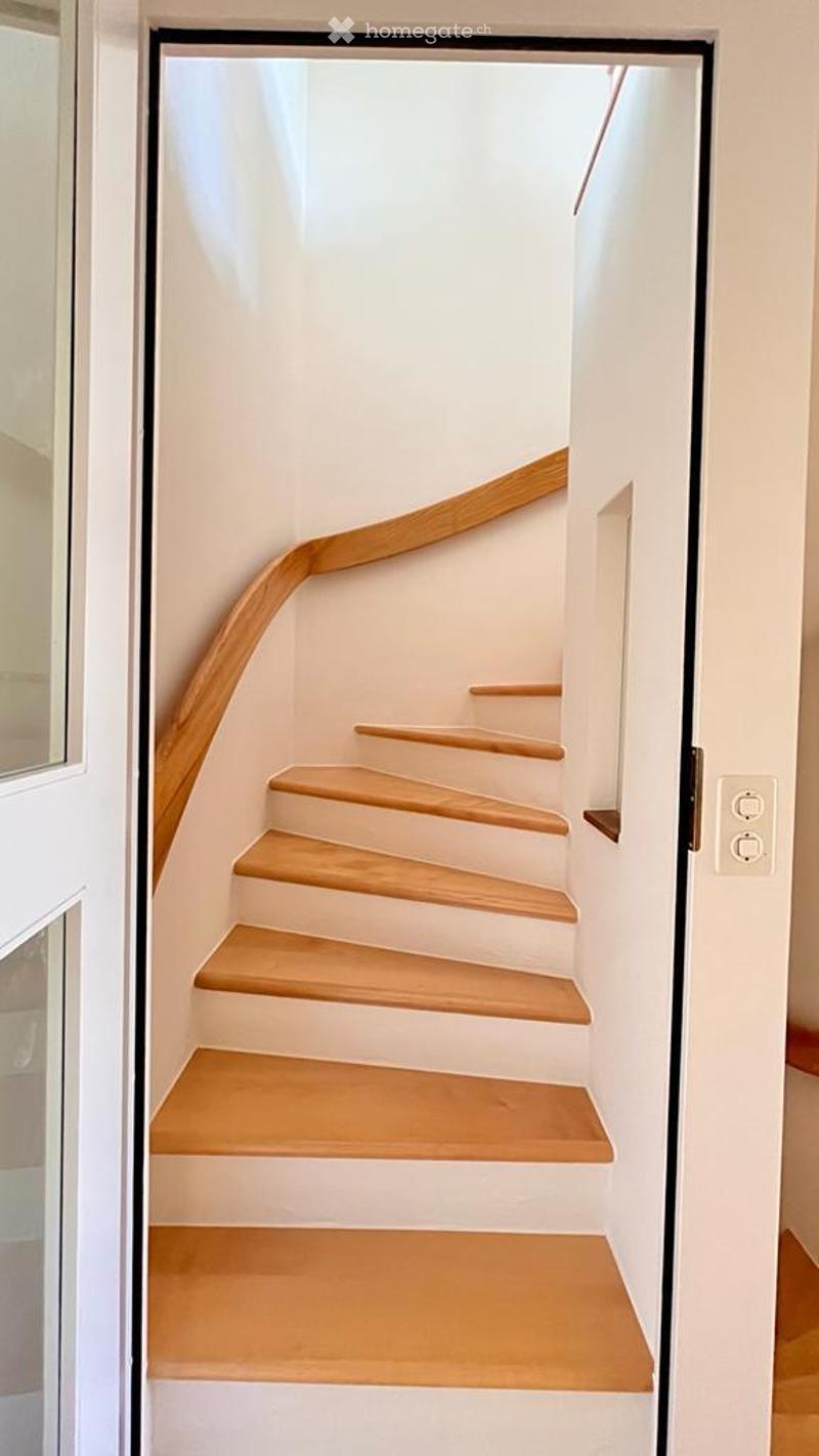 A modern staircase with wooden steps and a wooden handrail, leading to an upper floor.