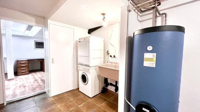 Laundry room with washing machine, dryer, sink, and water heater. Wooden desk and cabinet in the corner.