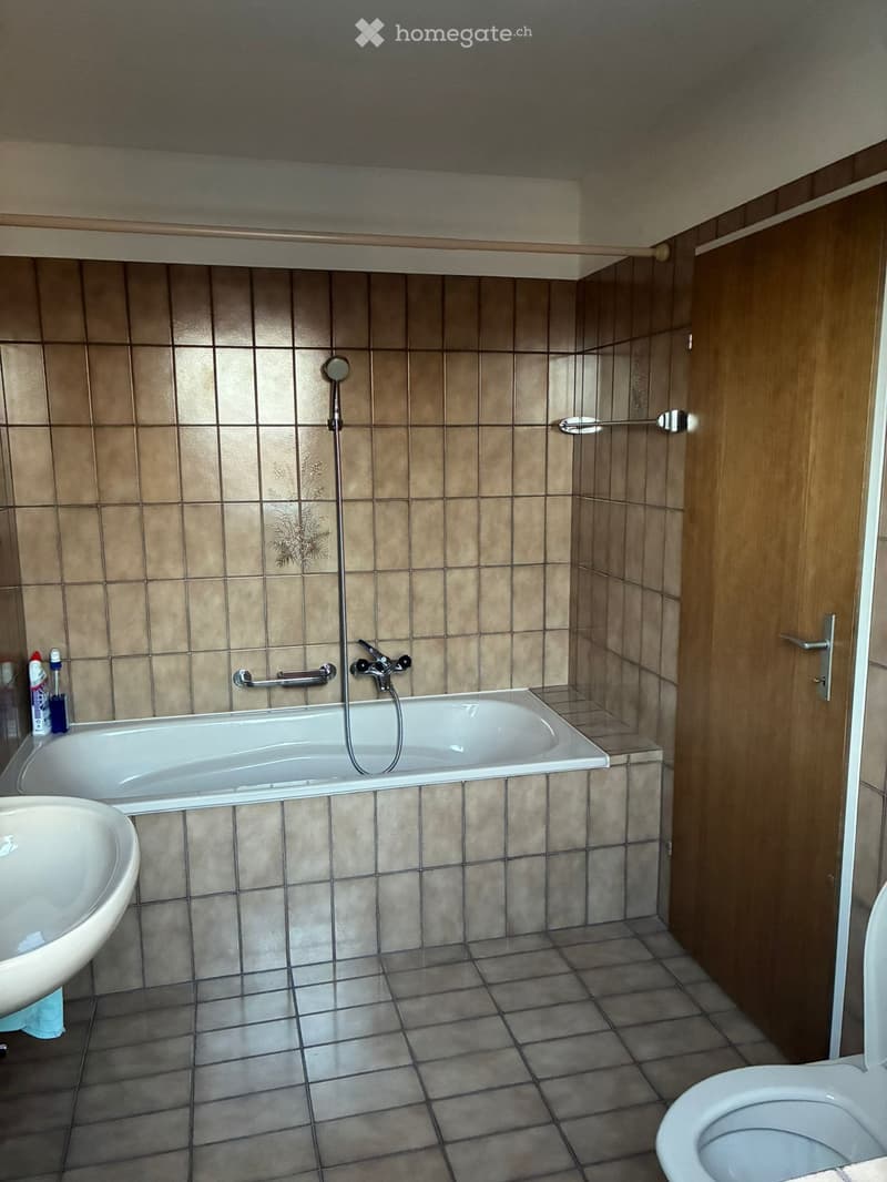 Bathroom with bathtub, sink, toilet, tiled walls and floor, shower head, and faucet