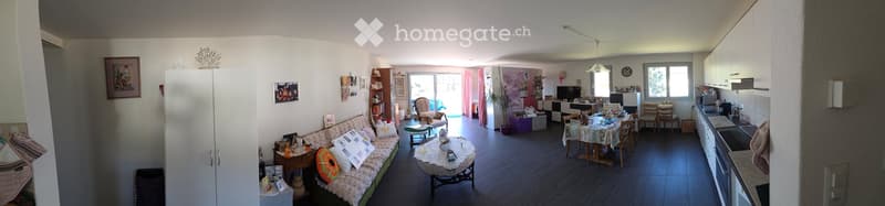 Furnished Room. A well-lit, open-plan living and dining area with a sofa, coffee table, dining table, chairs, and a small kitchen area with cabinets, refrigerator, microwave, and oven. The space features a mix of modern and traditional decor, including a