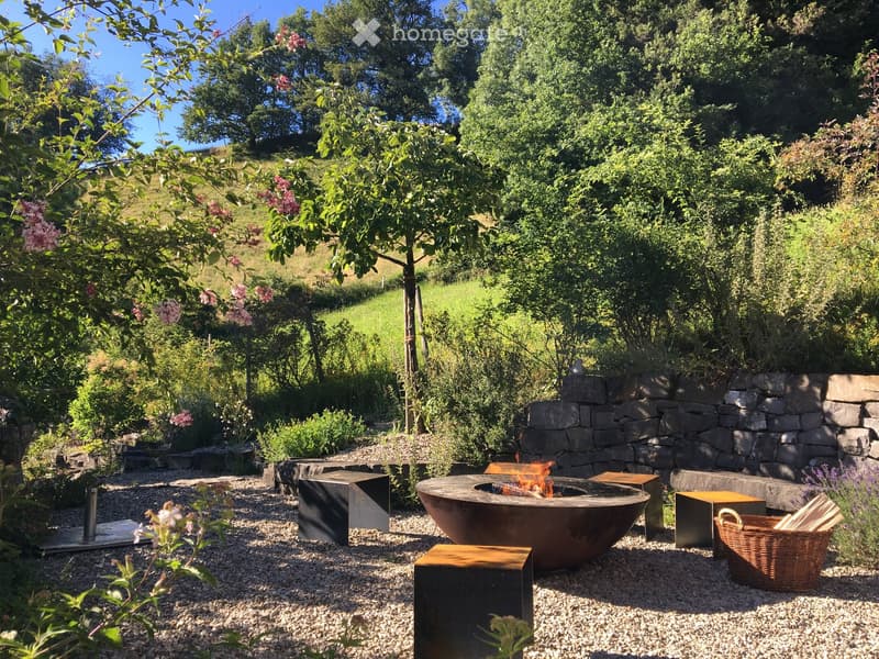 Outdoor area with a fire pit, wooden benches, and a basket of wood.