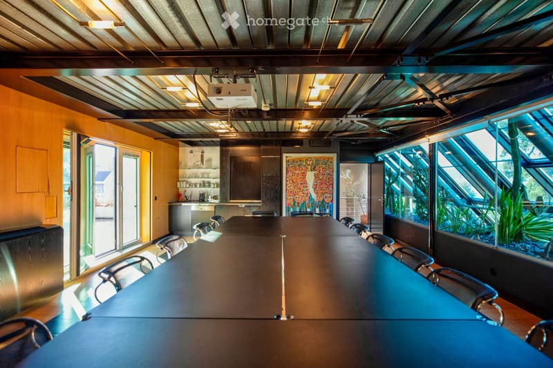 Modern, industrial-style room with a long conference table surrounded by chairs, a kitchen area with cabinets and a sink, and a large aquarium window showcasing aquatic plants.