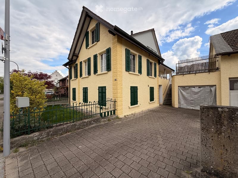Two-story yellow house with green shutters, a gated front yard, and a garage on the right side.