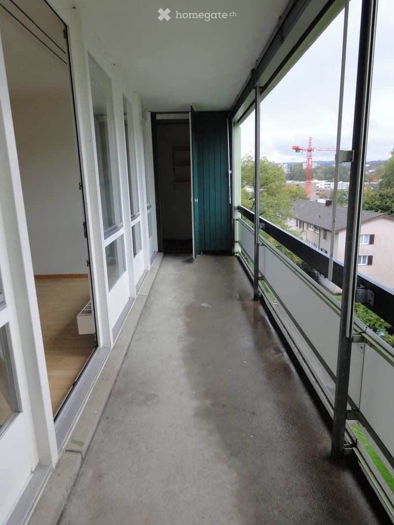 Balcony / Terrace. Empty balcony with concrete floor, large windows, and a view of the city and surrounding greenery.