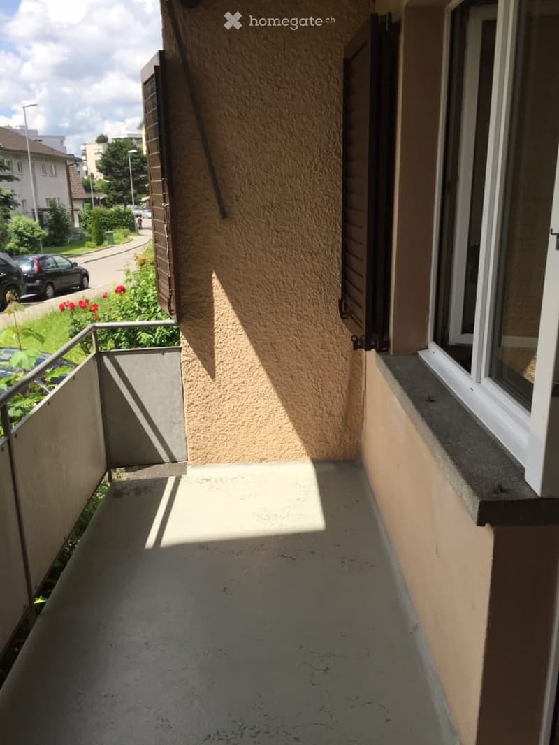 Balcony with metal railing, concrete floor, and a view of the street and neighboring buildings.