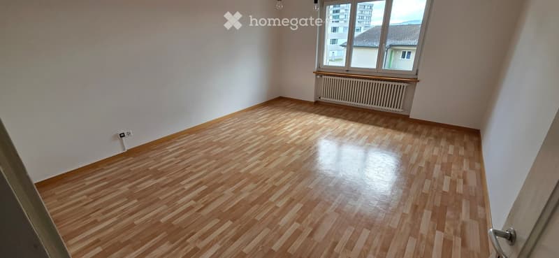 Empty room with wooden flooring, white walls, and a window with a radiator below it.