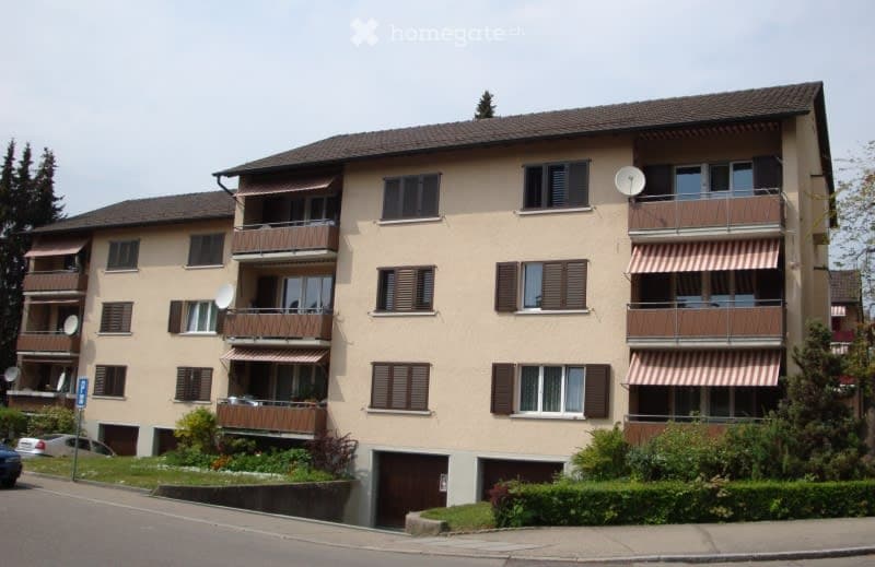 Multi-story residential building with beige facade, multiple balconies, and satellite dishes.