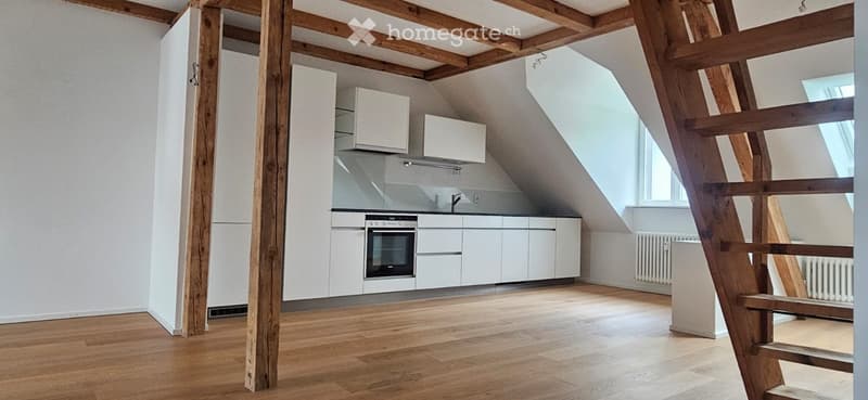 Modern kitchen with white cabinets, stainless steel appliances, and wooden flooring in an attic space.