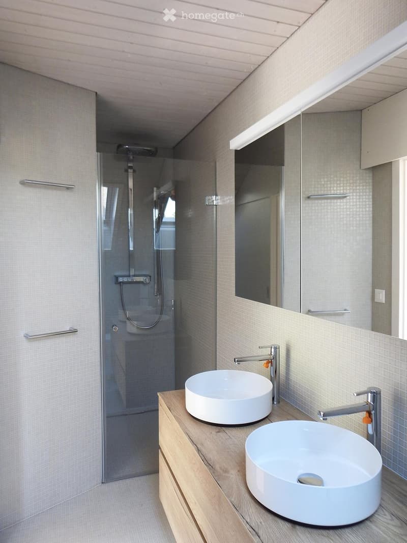 Modern bathroom with two white sinks on a wooden vanity, a large mirror, and a glass-enclosed shower area.