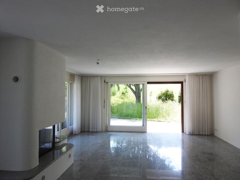 Empty room with polished concrete floor, large sliding glass doors leading to a garden, white walls, and built-in shelving unit on one side.