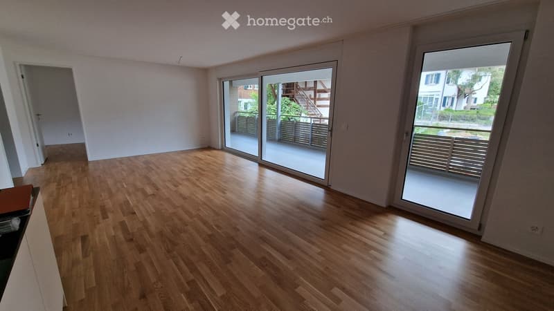 Empty room with wooden flooring, large sliding glass doors leading to a balcony, and white walls.