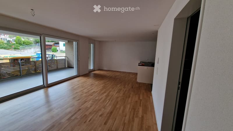 Empty room with wooden flooring, large sliding glass doors leading to a balcony, and a small built-in cabinet.
