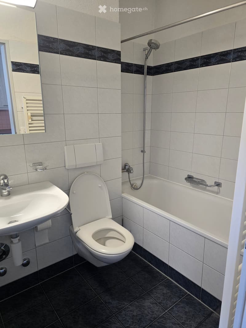 Modern bathroom with white tiles, black accents, toilet, sink, bathtub, and showerhead.