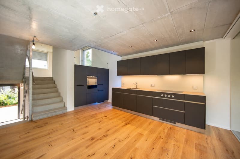 Modern kitchen with dark grey cabinets, wooden flooring, and built-in appliances including a stove and sink.