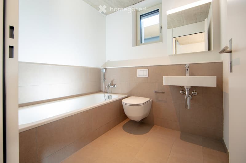 Modern bathroom with white walls, beige tiles, a toilet, a sink, and a bathtub. The bathroom appears to have a private washing machine and a dishwasher installed.