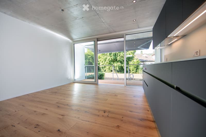 Open-concept living space with large windows, concrete ceiling, hardwood floors, and modern kitchen cabinets