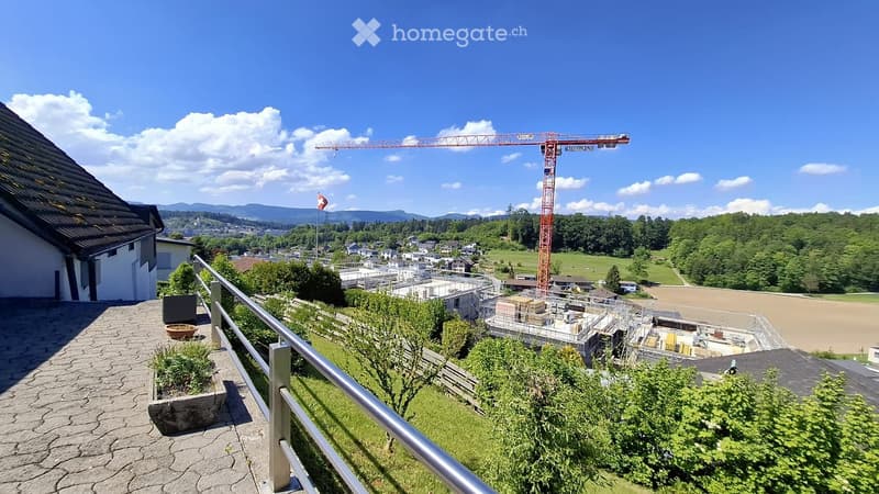 Balcony / Terrace. Balcony overlooking a town with a construction site, greenery, and a distant mountain range.