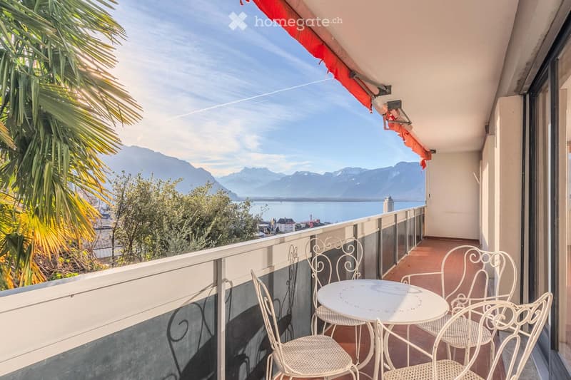 Balcony with a table and chairs, overlooking a scenic view of mountains and a lake.