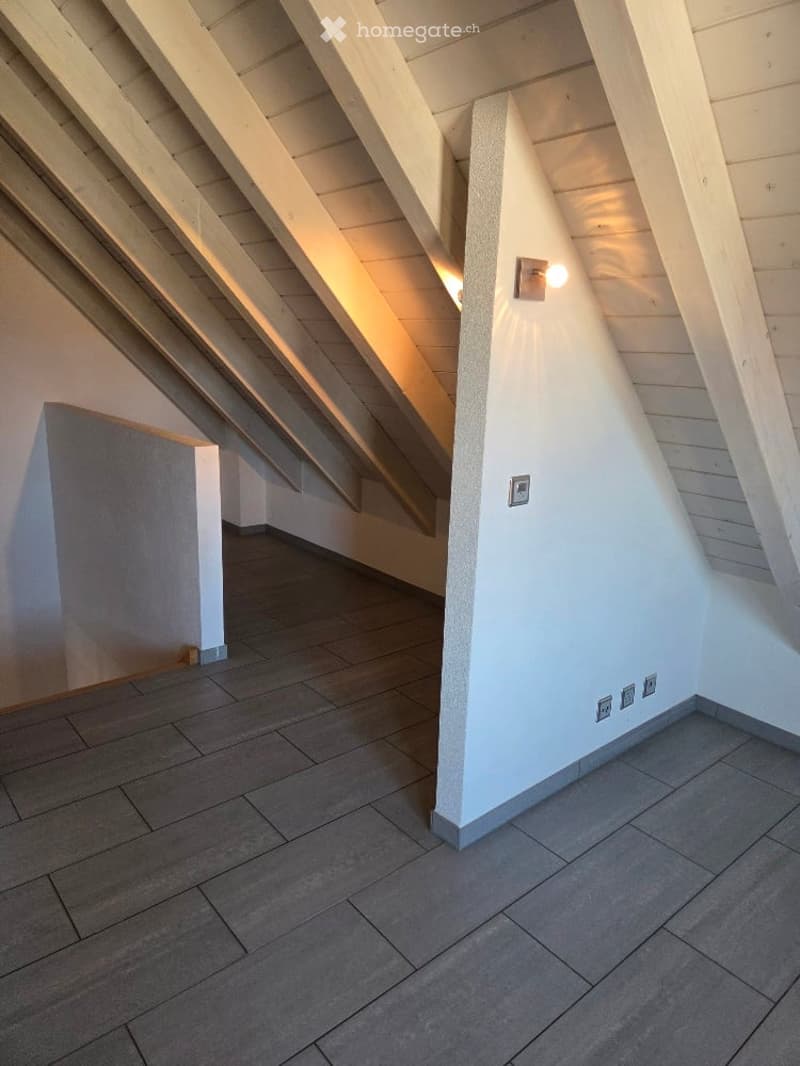 Empty attic room with wooden ceiling and tiled floor, illuminated by a light on the wall
