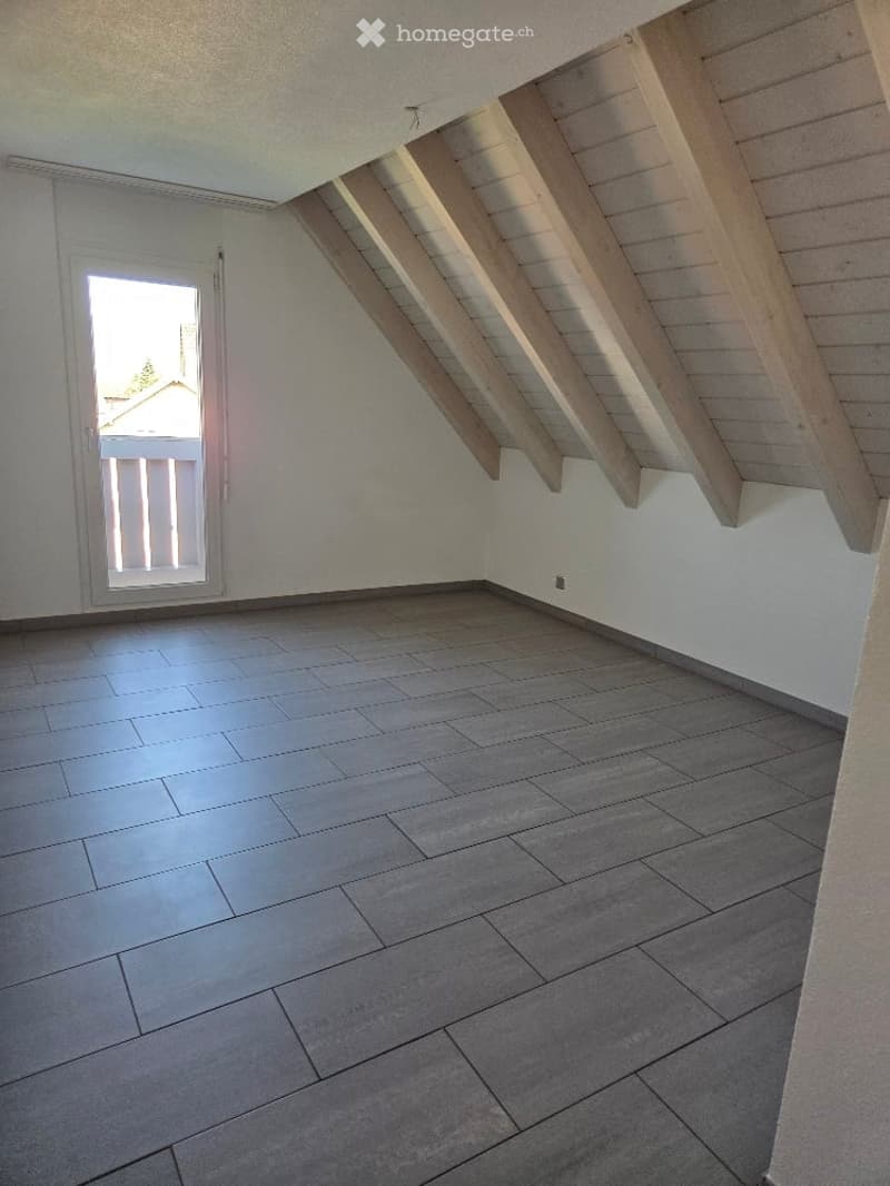 Empty room with gray tiles, wooden beams, glass door to balcony