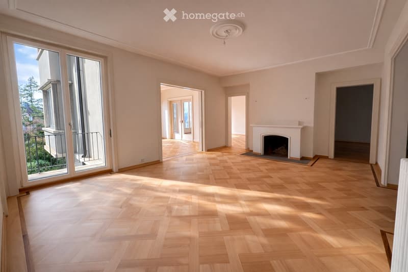 Empty room with wooden flooring, large windows, and a fireplace. No furniture or equipment present.