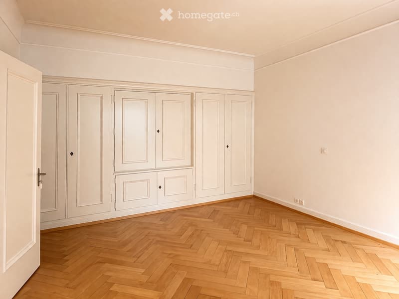 Empty room with wooden parquet floor, white walls, built-in wardrobes, and power outlets.