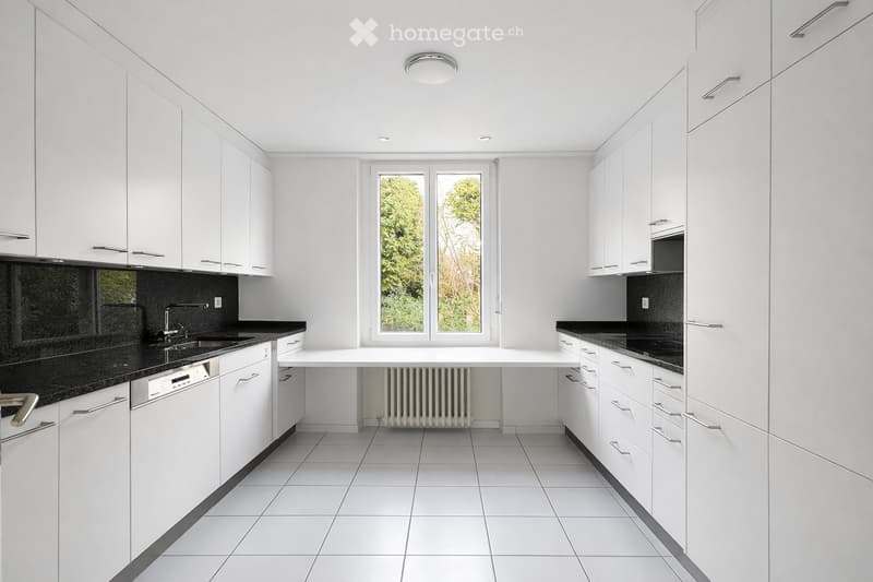 Modern kitchen with white cabinets, black countertops, and a large window overlooking greenery.