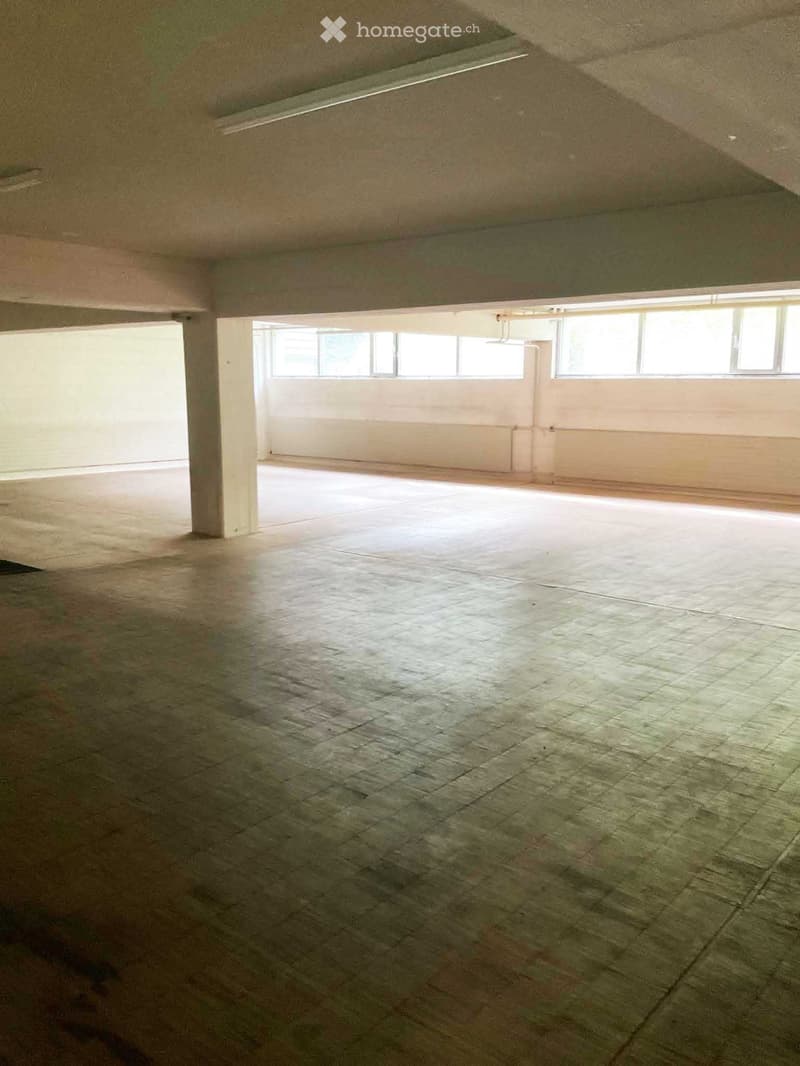 Empty room with concrete floors, white walls, and large windows allowing natural light. No furniture or equipment present.