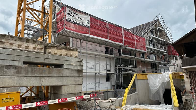 Multi-story building under construction with scaffolding, concrete supports, and a large banner on the facade.